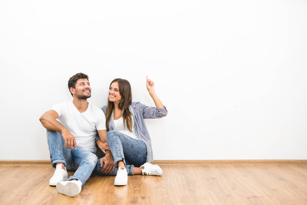The happy man and woman sit on the background of the white wall - Photo, Image