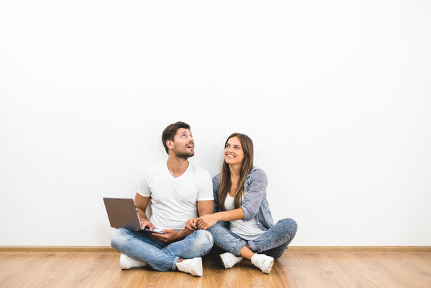 The happy man and woman with a laptop sit near the empty wall - Foto, Bild