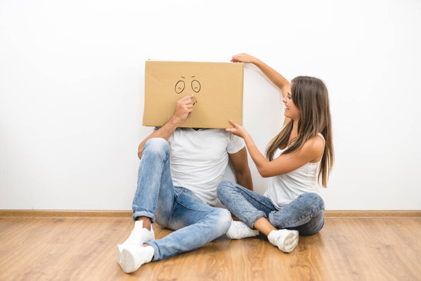 Мужчина с коробкой на голове сидит рядом с женщиной - Фото, изображение