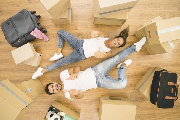 The smile couple lay on the floor and thumb up near boxes. view from above - Foto, Bild