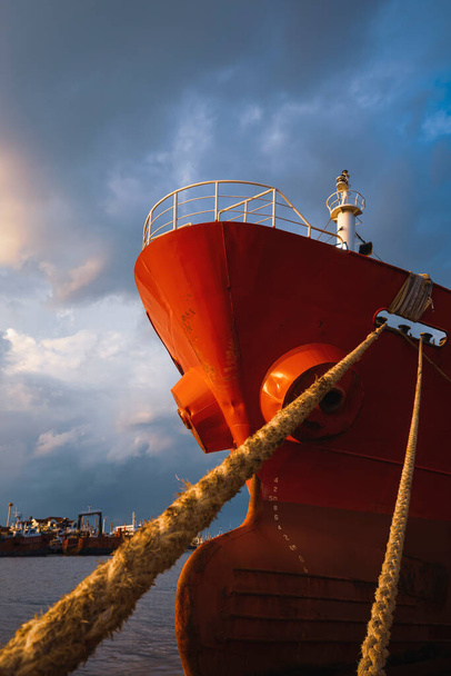 Low angle view of cargo ship docked at port against rain cloudy sky at sunset time in vertical frame - Photo, Image