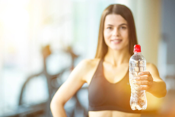 La joven sostiene una botella de agua en el gimnasio - Foto, imagen