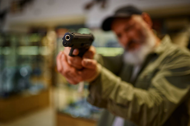 Бородач целится пистолетом в оружейный магазин. - Фото, изображение