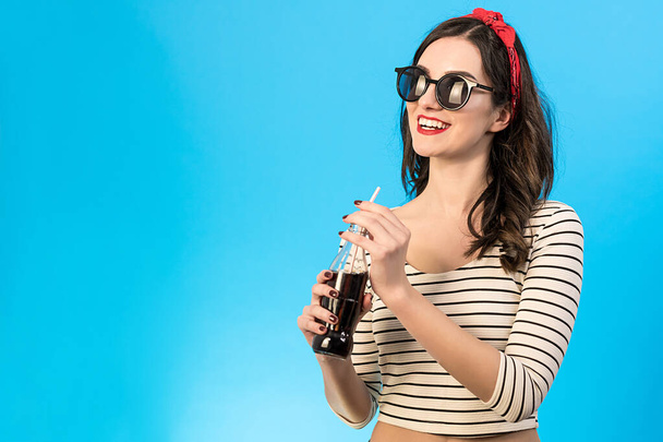 La donna felice in occhiali da sole che beve una cola sullo sfondo blu - Foto, immagini
