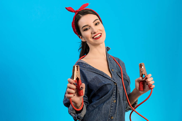 Жінка-механік тримає кабелі-перемички на синьому фоні
 - Фото, зображення