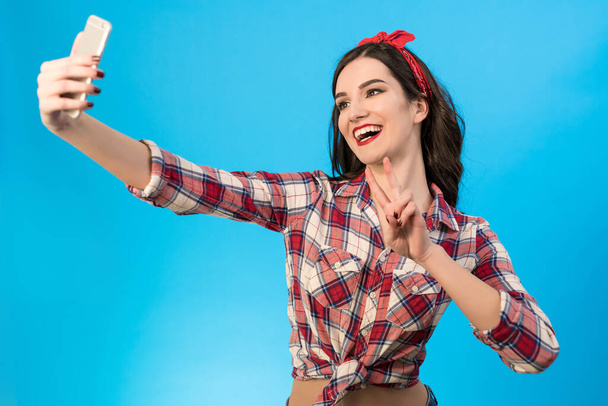 The cute woman makes a selfie on the blue background - Photo, Image