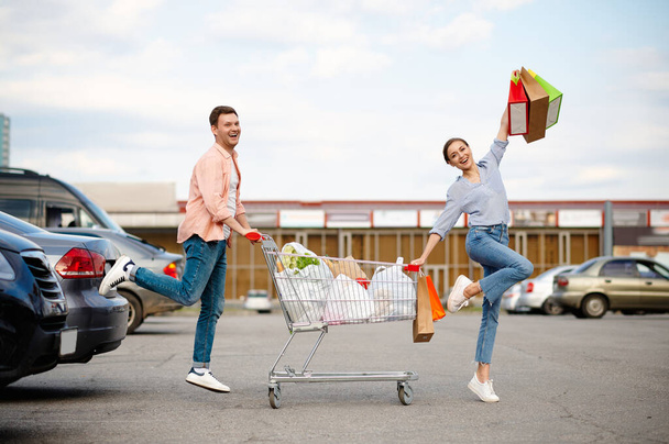 Cheerful family couple with cart on car parking - Fotografie, Obrázek