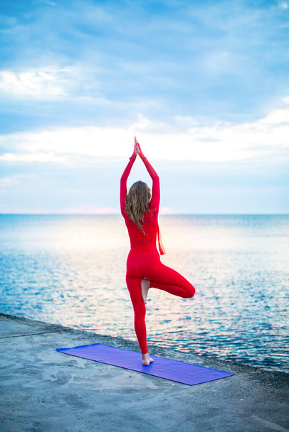 yoga asana à une jambe, sur le remblai près de la mer à l'aube avec des nuages dans le ciel - Photo, image