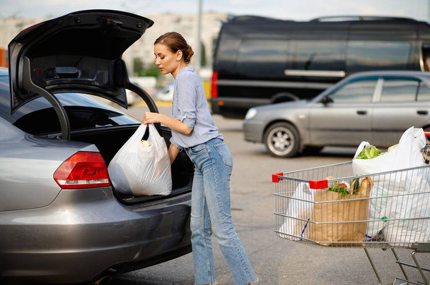vrouw met kar zet haar aankopen in auto kofferbak - Foto, afbeelding