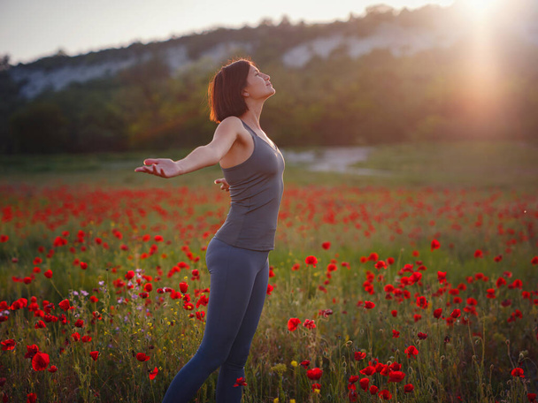 Young beautiful woman with raised arms in spring poppy field. Soft colors. pensive relaxed atmosphere. - Photo, Image