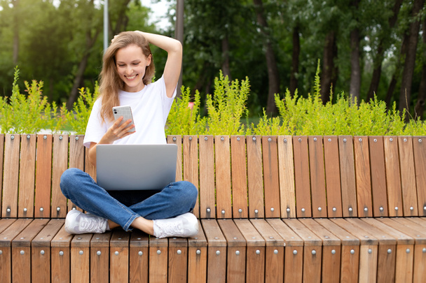 Ευτυχισμένη κομψή γυναίκα blogger γελάει ενώ συνομιλεί με φίλους σε κοινωνικά δίκτυα στη συσκευή laptop. νεαρή γυναίκα ανάγνωση ευχάριστο μήνυμα κειμένου από τον καλύτερο φίλο συνδέεται με το δημόσιο διαδίκτυο σε εξωτερικούς χώρους - Φωτογραφία, εικόνα