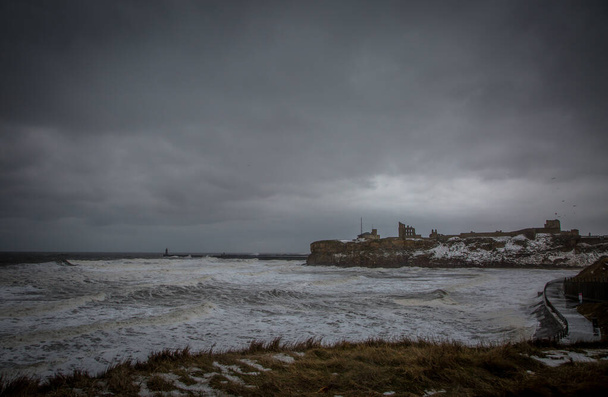 Las olas gigantes golpean la bahía del rey Eduardo durante una tormenta de invierno, ya que los acantilados circundantes del Priorato de Tynemouth están cubiertos con un chorro de nieve. - Foto, Imagen