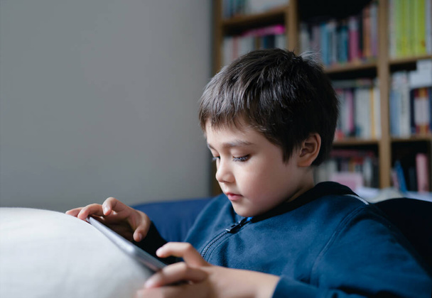 Portrait kid lying on sofa watching cartoon on tablet, Cute boy playing game on touch pad, Child having fun and relaxing on his own in study room, New normal lifestyle - Foto, immagini