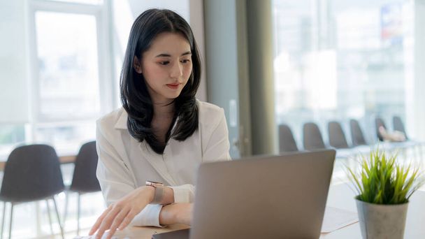 Beyaz gömlekli Asyalı kendine güvenen iş kadını modern ofisteki dizüstü bilgisayar üzerinde sıkı çalışıyor.. - Fotoğraf, Görsel