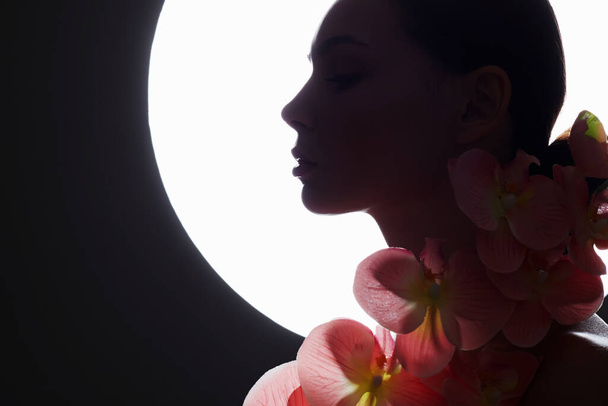 Hermosa mujer joven con flor de orquídea. silueta femenina con flores en el fondo de la luna - Foto, Imagen