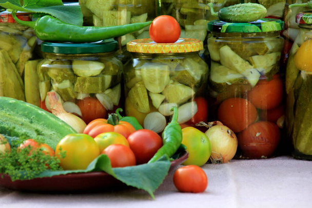 Säilyttää vihanneksia lasipurkeissa pöydällä kesäpuutarhassa. lasipurkit eri vihanneksia. Marinoitua ruokaa.Purkit marinoituja vihanneksia puutarhassa. - Valokuva, kuva