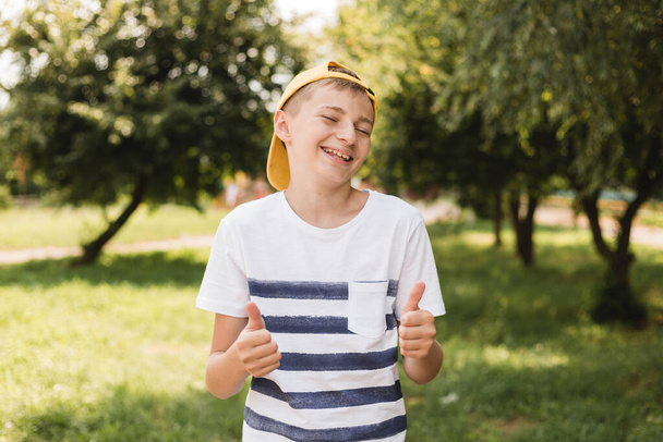 Teenage smile boy showing thumb up gesture on nature background, gesture concept. Boy wearing on stripe t-shirt and yellow hat - Fotoğraf, Görsel