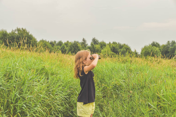 the child girl stands in a meadow and looks through binoculars - Foto, immagini