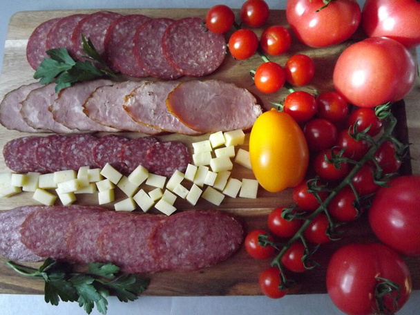slicing smoked sausage of four varieties with cheese and red and yellow tomatoes and cherry tomatoes - Photo, Image