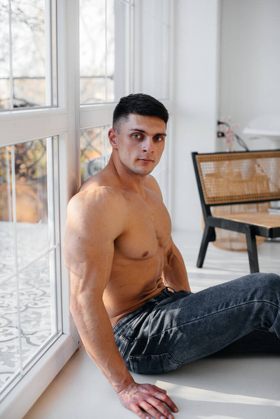 A young sexy athlete with perfect abs poses in the studio topless in jeans on the background. Healthy lifestyle, proper nutrition, training programs and nutrition for weight loss. - Fotó, kép