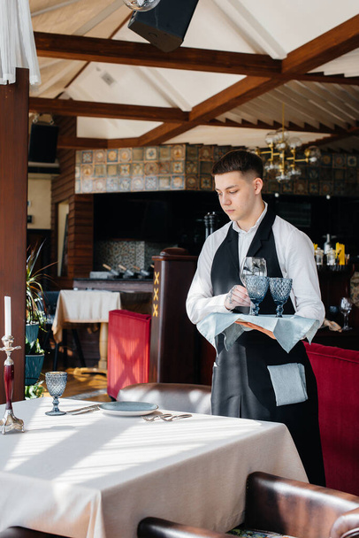 A young male waiter in a stylish uniform is engaged in serving the table in a beautiful gourmet restaurant. Restaurant activity, of the highest level. - Foto, imagen