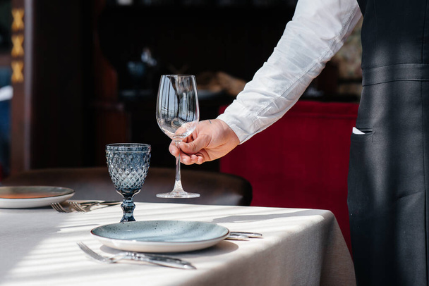 A young waiter in a stylish uniform is engaged in serving the table in a beautiful gourmet restaurant close-up. Restaurant activity, of the highest level. - Valokuva, kuva