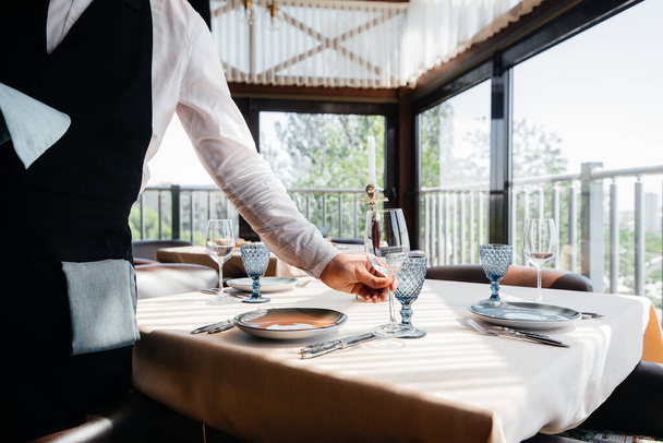 A young waiter in a stylish uniform is engaged in serving the table in a beautiful gourmet restaurant close-up. Restaurant activity, of the highest level. - Foto, Imagem