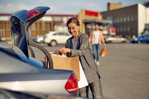 Mulher coloca suas compras no porta-malas no estacionamento - Foto, Imagem
