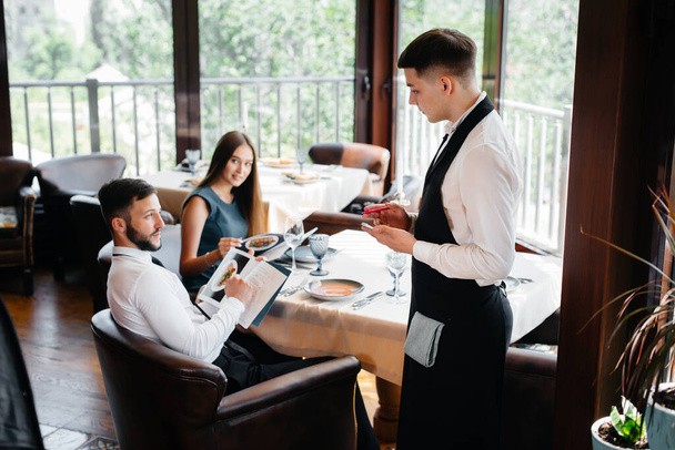 A stylish waiter serves a young couple who came on a date in a gourmet restaurant. Customer service in the catering. - Valokuva, kuva
