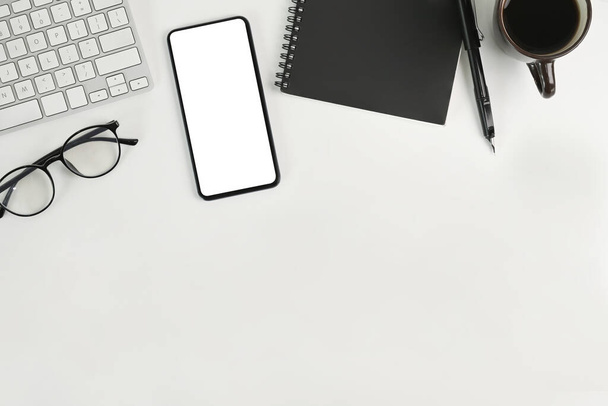 Mock up smartphone, notebook, koffiebeker en glazen op wit bureau. - Foto, afbeelding