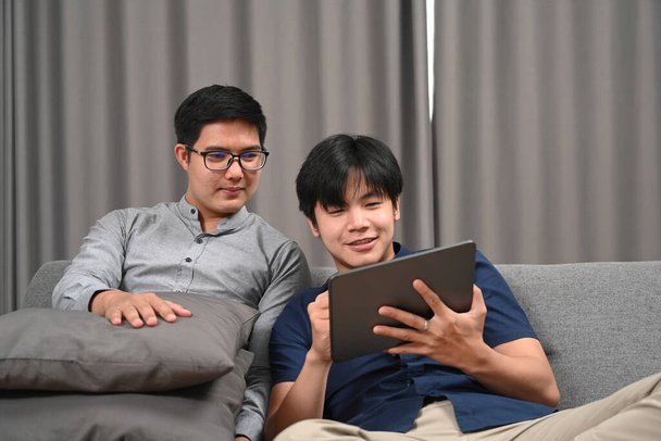 Couple homosexuel utilisant numérique ensemble sur canapé confortable. - Photo, image