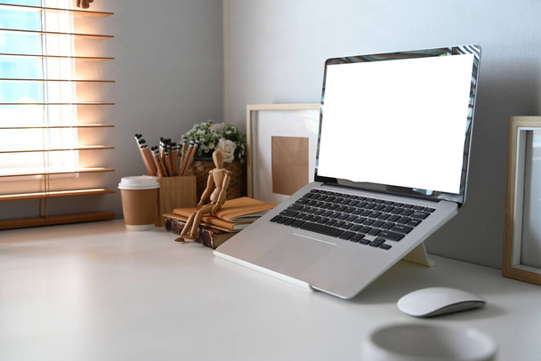 Computador portátil com tela em branco, planta de sala, porta-lápis e xícara de café na mesa branca no escritório em casa. - Foto, Imagem