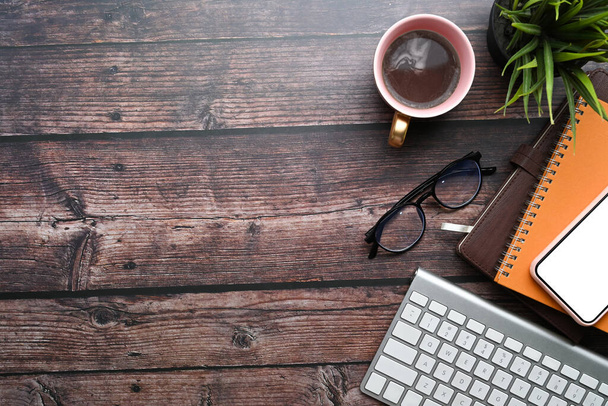 Smart phone, coffee cup, notebook, glasses, keyboard on wooden table. - Photo, Image