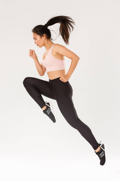 Sport, gym and healthy body concept. Full length of serious focused female runner, motion shot of girl running in air, fitness training of cute slim sportswoman, athlete workout in active wear - Photo, Image