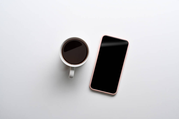 Draufsicht auf Handy-Attrappe und Kaffeetasse auf weißem Hintergrund. - Foto, Bild