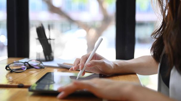 Közelkép az üzletasszony kezében stylus toll írás digitális táblagépen, miközben ül az ablak közelében az irodában. - Fotó, kép