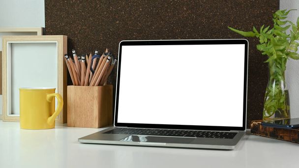 Fermez l'ordinateur portable avec écran blanc, porte-crayon, tasse à café et plante d'intérieur sur la table blanche. - Photo, image