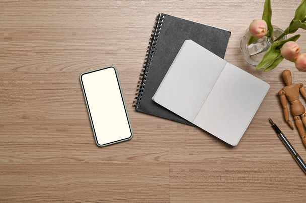 Above view of smart phone and empty notebook on wooden background. - Foto, afbeelding