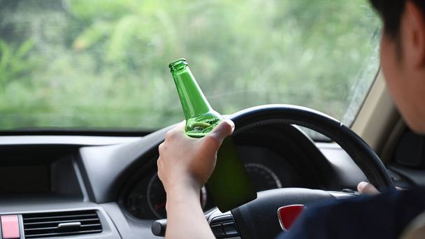 Homme conduisant une voiture tout en tenant une bouteille de bière. Conduire sous l'influence.  - Photo, image