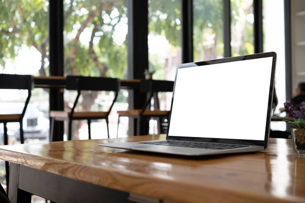 Computadora portátil con pantalla blanca en escritorio de madera en la cafetería moderna. - Foto, Imagen