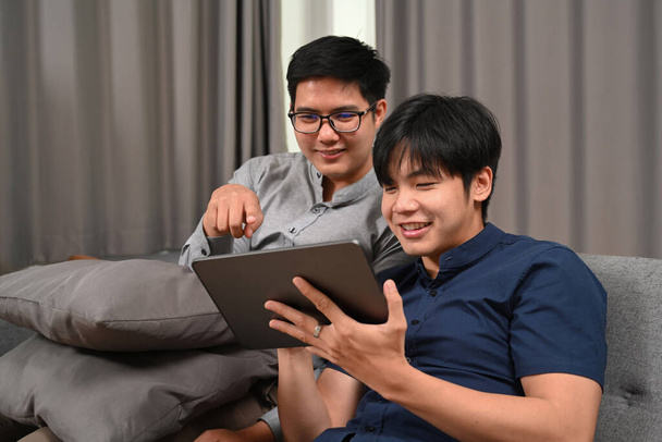 Ázsiai homoszexuális pár szörfözik az interneten digitális, miközben ül a kanapén. Homoszexuális, LMBT-koncepció. - Fotó, kép