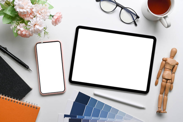 Vista superior de mock up tablet digital, telefone celular, óculos, notebook e xícara de café na mesa branca. - Foto, Imagem