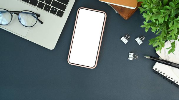 Модели мобильного телефона с пустым экраном и ноутбуком на рабочем столе. - Фото, изображение