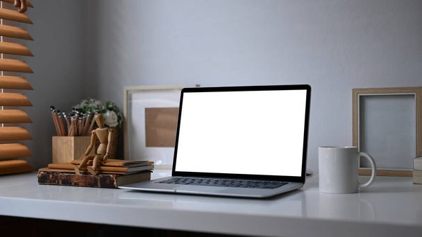 Computer laptop met blanco scherm, kamerplant, potloodhouder en koffiebeker op wit bureau bij raam. - Foto, afbeelding