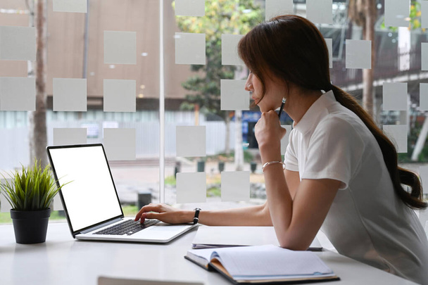 Вид збоку жінки-підприємця зосереджений на роботі на ноутбуці, сидячи на сучасному робочому місці
. - Фото, зображення