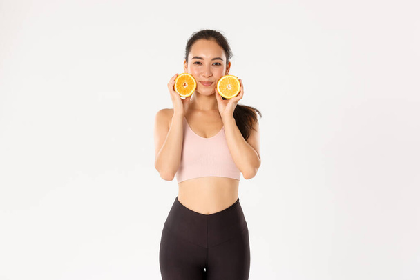 Sport, pohoda a aktivní životní styl koncepce. Hloupé a roztomilé asijské fitness dívka, ženský atlet hubnutí s cvičením, tělocvična tréninky a zdravá strava, ukazuje dvě poloviny pomeranče - Fotografie, Obrázek