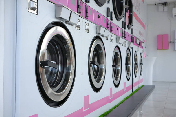 Row of washing machines in a public laundromat. Self service laundry facilities. - Zdjęcie, obraz