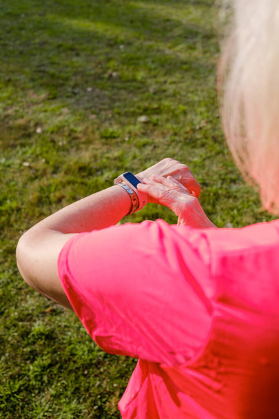 Sportliche Seniorin checkt beim Training ihre Smartwatch. Vertikales Foto. - Foto, Bild