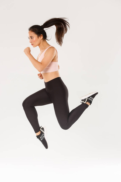Sport, gym and healthy body concept. Full length of serious focused female runner, motion shot of girl running in air, fitness training of cute slim sportswoman, athlete workout in active wear - Foto, Imagem