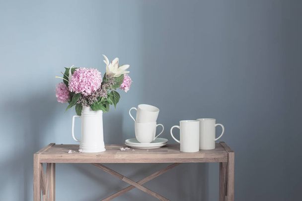 white cups and flowers on vase  on wooden shelf on gray background - Foto, Imagem